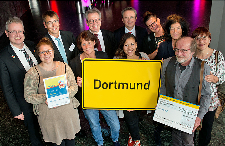 Eine Gruppe, die das Ortsnamensschild Dortmund trägt, lächelt in die Kamera.
